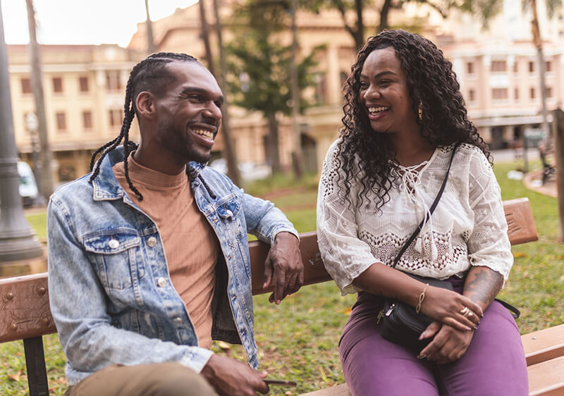 Two people sitting on a bench smiling and talking with one another